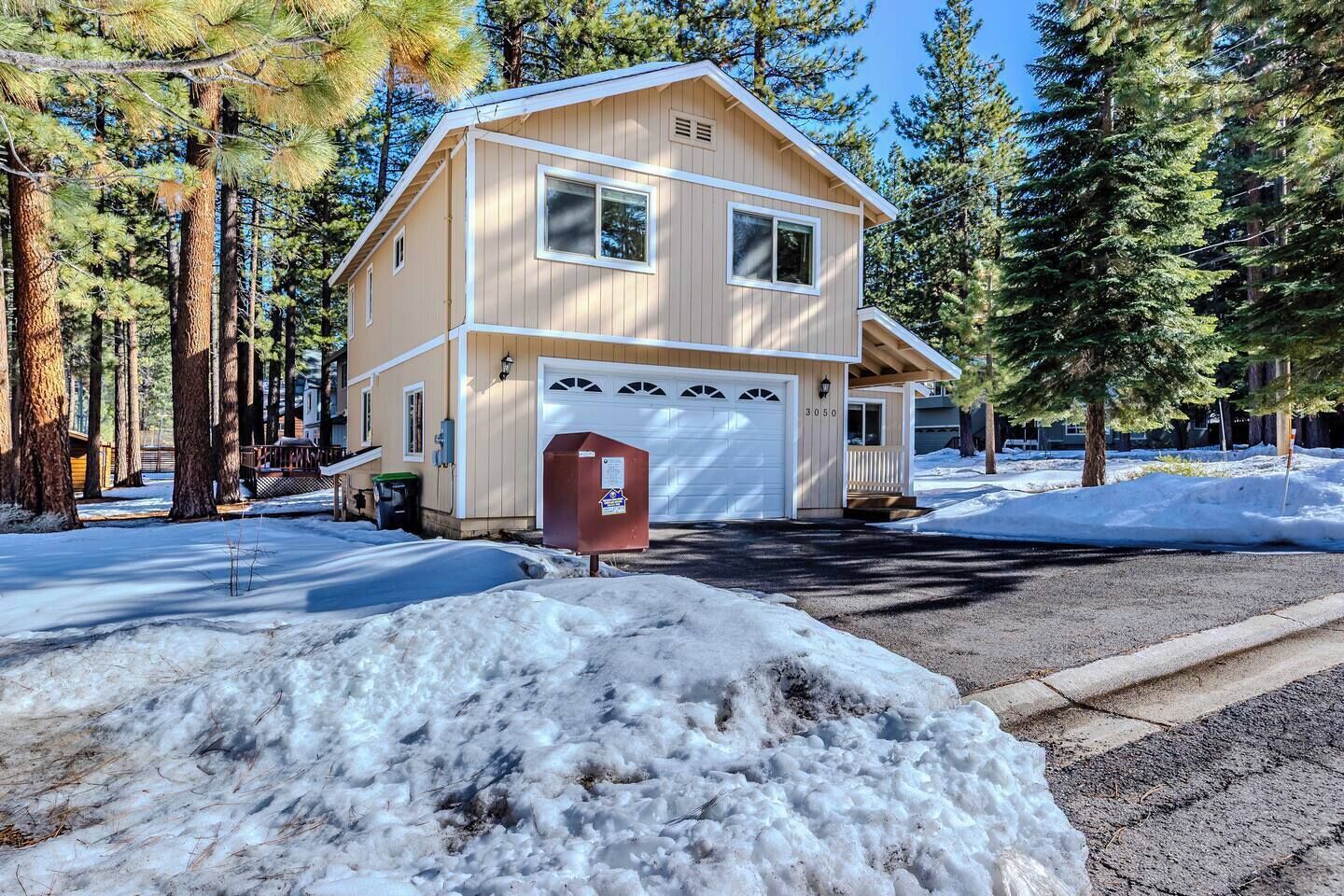 A two-story building with a garage, surrounded by trees and covered in snow.