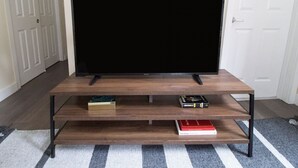 Litteänäyttöinen televisio on sijoitettu puiseen TV-telineeseen, jossa on kaksi hyllyä, ja kummallakin hyllyllä on yksi kirja.