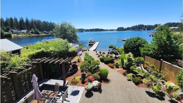 Eine Terrasse mit Gartenmöbeln, einer Holzpergola und Blick auf einen See mit Booten.