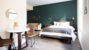 Ett modernt hotellrum med en säng, ett litet skrivbord, en stol och en rund spegel.
