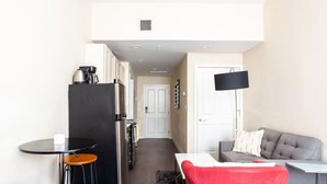 A compact living space with a kitchenette, a dining area with stools, a sofa, and a TV mounted on the wall. - Center of Boston Studio Pet Friendly | Laundry (Boston)