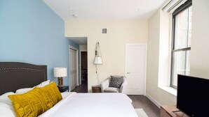 A hotel room with a bed, a TV, a chair, and a window. - Downtown Luxury 1BR | Pets Welcome | W/D in Bldg (Boston)