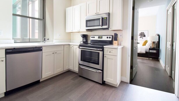 A modern kitchen with white cabinets, a stainless steel dishwasher, a microwave, and an oven. - Downtown Luxury 1BR | Pets Welcome | W/D in Bldg (Boston)
