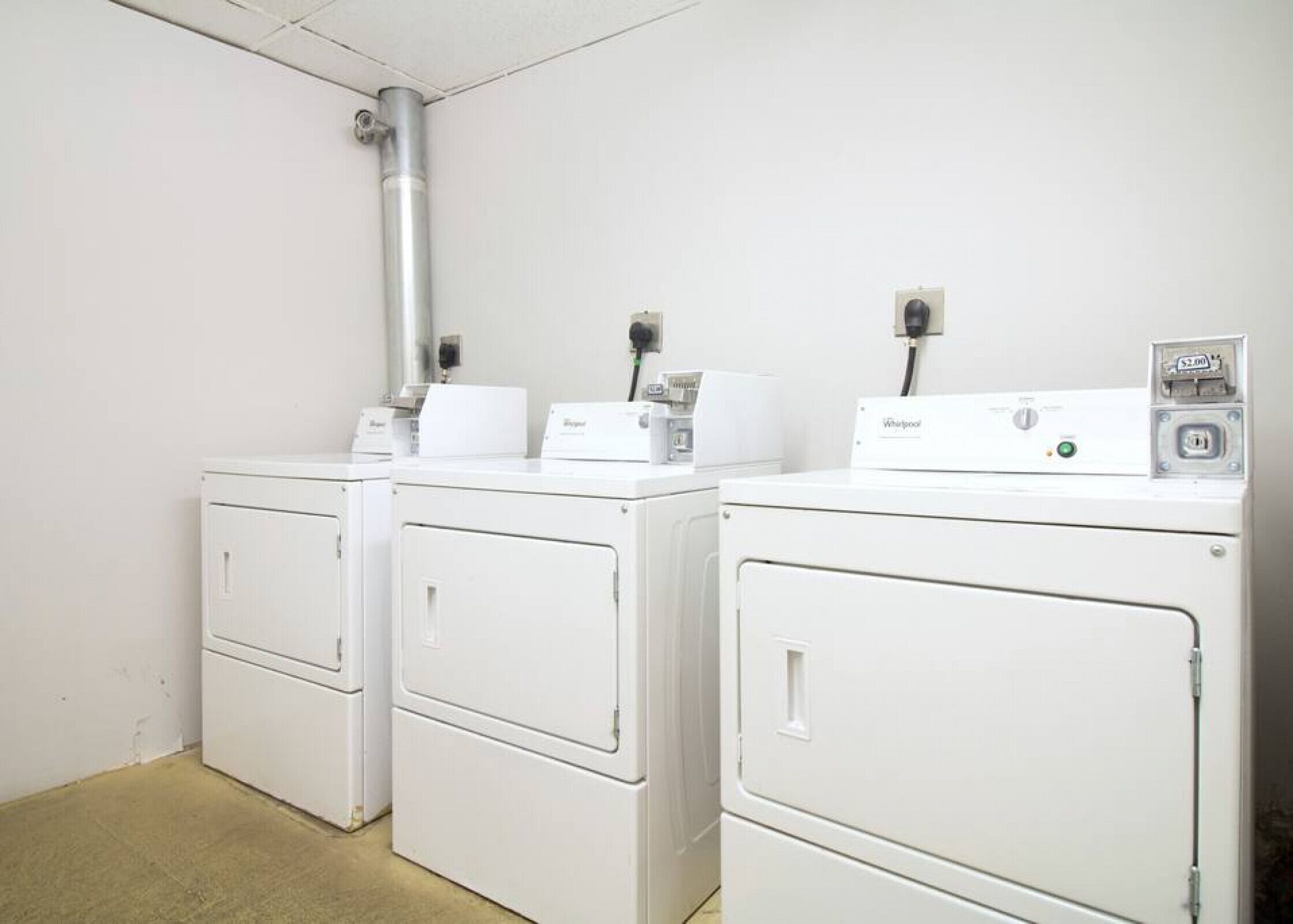 A laundry room with two white Whirlpool washers and dryers, a metal vent, and a power outlet.