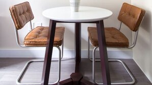 A small, round table with a white top and a single white vase with green foliage. Two brown leather chairs with metal frames are positioned on either side of the table. - Studio walking distance to MGH and Tufts Medical (Boston)