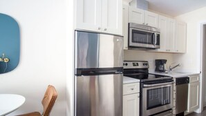 A modern kitchen with stainless steel appliances, white cabinetry, and a blue wall clock. - Studio walking distance to MGH and Tufts Medical (Boston)