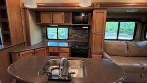 A compact RV kitchen with a central island, built-in microwave, and a stove.