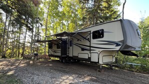 A recreational vehicle parked on a gravel path surrounded by trees.