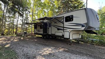 A recreational vehicle parked on a gravel path surrounded by trees.