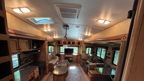 A well-lit RV interior with a kitchen, dining area, and seating space.
