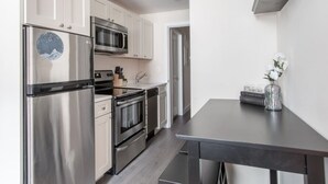 Una cocina moderna con electrodomésticos de acero inoxidable, armarios blancos y encimera oscura.