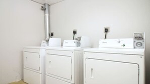 Un cuarto de lavandería con dos lavadoras y secadoras Whirlpool blancas, un conducto de ventilación metálico y un enchufe en la pared.