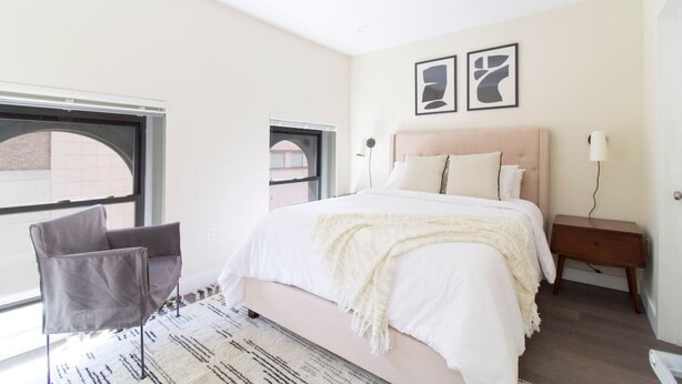 A modern bedroom with a large bed, a chair, a nightstand, and two abstract wall art pieces. - Downtown Boston | Nurses Welcome | W/D in bldg (Boston)