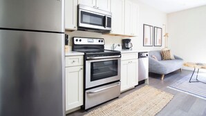 A modern kitchen with stainless steel appliances, white cabinetry, and a grey sofa in the living area. - Downtown Boston | Nurses Welcome | W/D in bldg (Boston)