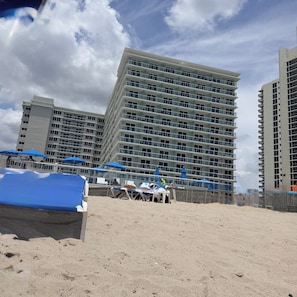 Een hotel aan het strand met meerdere verdiepingen, terraszitplaatsen en parasols.