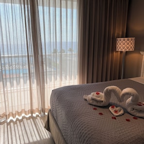 Een hotelkamer met een bed, dunne gordijnen, een lamp en uitzicht op zee.