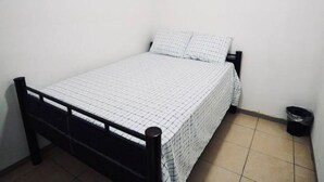 A small, single-bed room with a plain white wall, a black metal frame, and a white checkered bedspread. - Hostel 101 (Mazatlán)
