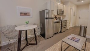 A compact kitchen with stainless steel appliances, a dining area with wire chairs, and a small table. - Serene Studio | Close to MGH (Boston)