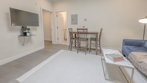 Ett modernt vardagsrum med en platt-TV, ett matbord med stolar, en blå soffa och en vit matta.
