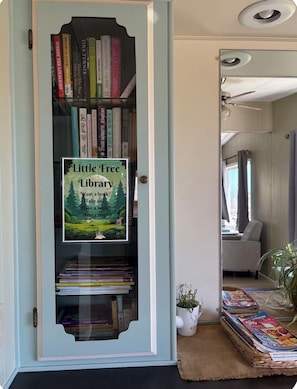 A bookshelf with a 'Little Free Library' sign, a potted plant, and magazines on a table. - Coastal Retreat With Bay Views (Eureka)