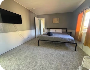 A bedroom with a bed, a television mounted on the wall, and a door leading to another room. - Coastal Retreat With Bay Views (Eureka)