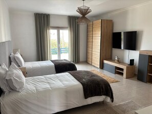 Ein Schlafzimmer mit zwei Betten, einem Fernseher, einem Kleiderschrank und Blick auf einen Balkon.