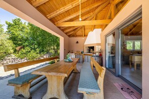 An outdoor patio with wooden benches and a stone wall, leading to a glass door entrance. - Villa ULIKA with private pool and sauna (Malinska)