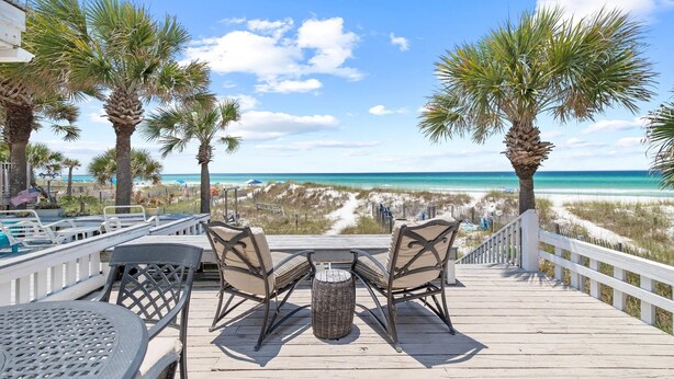 A wooden deck with outdoor seating and a view of the beach.