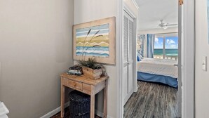 A bedroom with a bed, a nightstand, a painting, and a view of the ocean.