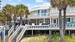 A beachfront property with a wooden deck, multiple balconies, and palm trees.