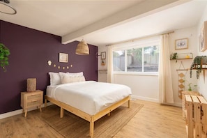 A bedroom with a wooden bed, a window with curtains, a bedside table, and a wall-mounted shelf with plants. - Boho Retreat w/ Covered Patio & Stylish Vibes (SeaTac)