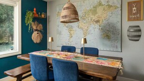 Een eetgedeelte met een houten tafel, blauwe stoelen, een wereldkaart, een hanglamp en een wereldbol aan de muur.