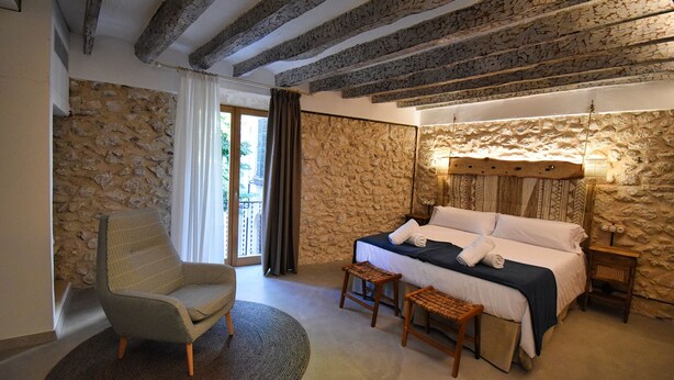 Une chambre avec des murs en pierre, un lit recouvert de draps blancs, une chaise et une petite table.