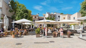 Un café en plein air avec des tables et des chaises sous des parasols, entouré d’immeubles et d’arbres.
