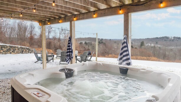 A hot tub with a stone wall backdrop, outdoor seating, and a view of a snowy landscape.