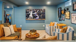 A living room with a large TV displaying a sports event, a coffee table with a board game, and two sofas with striped cushions.