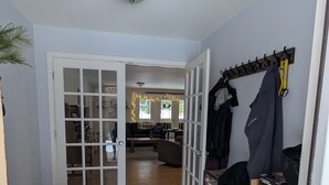 Un pasillo con una puerta que da a una sala de estar, un perchero con chaquetas y un zapatero con varios calzados.