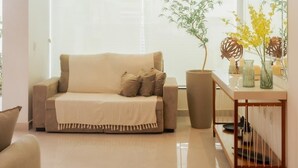 A modern living room with a beige sofa, a large window, and a small table with decorative items. - @durhambeachhouse your vacation home in Porto Seguro. Comfort and privacy. (Porto Seguro)