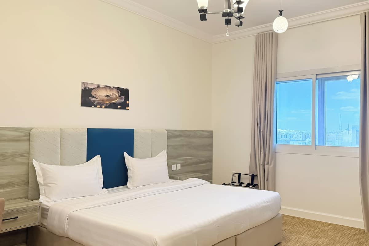 Una habitación de hotel con cama, mesita de noche, lámpara de pared, cortinas en la ventana y vistas a la ciudad.