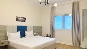 A hotel room with a bed, a nightstand, a wall-mounted lamp, a window with curtains, and a cityscape view.