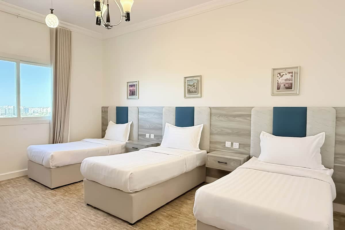 Habitación de hotel con dos camas individuales, un escritorio pequeño, una mesita de noche y una ventana con cortinas.