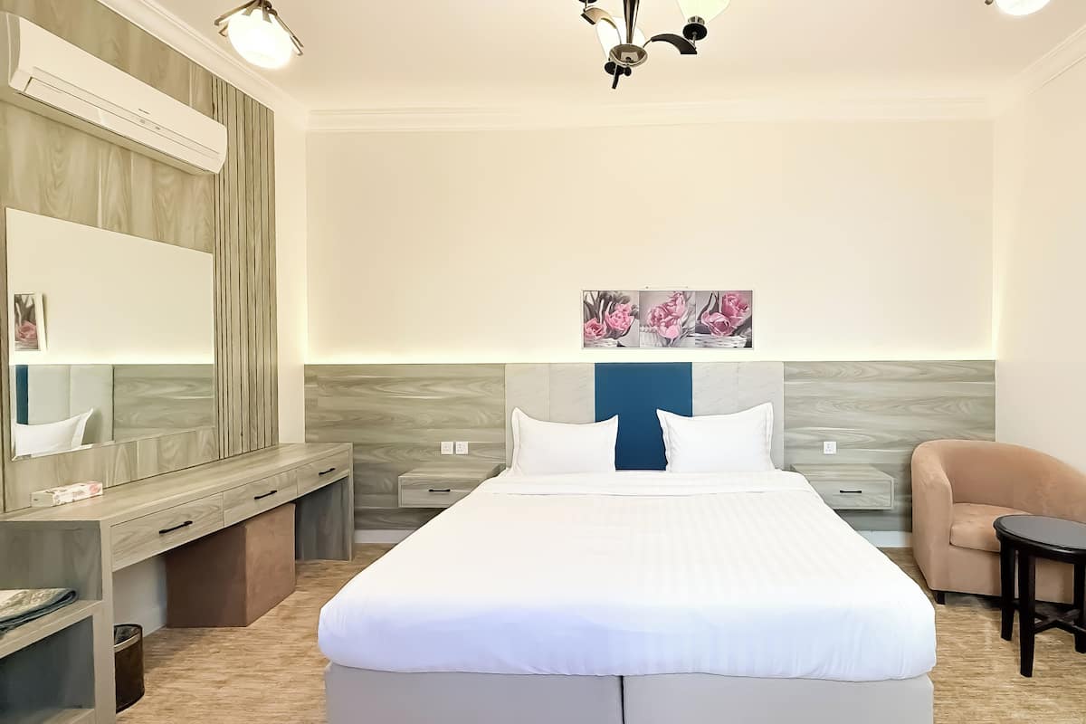Habitación de hotel con una cama grande, mesitas de noche, una silla, un escritorio, un espejo y una lámpara en el techo.