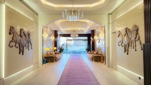 A luxurious hallway with a central chandelier, a purple carpet, and horse-themed wall art. - Sadeem Al Fkhr (Taif)
