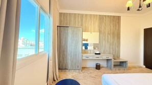 A hotel room with a large window, a bed, a desk with a mirror, and a wardrobe. - Sadeem Al Fkhr (Taif)