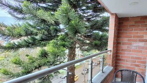 A balcony with a metal railing, a table, and chairs. A large tree is visible in the background. - Modern, 3-bedroom, elegant apartment in the best location 402 (Medellín)