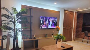 A modern living room with a flat-screen TV mounted on the wall, a wooden coffee table with a vase of flowers, and a potted plant. - Modern, 3-bedroom, elegant apartment in the best location 402 (Medellín)
