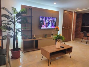 A modern living room with a flat-screen TV mounted on the wall, a wooden coffee table with a vase of flowers, and a potted plant. - Modern, 3-bedroom, elegant apartment in the best location 402 (Medellín)
