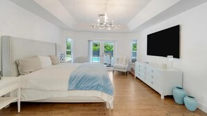 A spacious bedroom with a large bed, a dresser, a TV, and a view of the outdoors. - The Gardens Estate - Luxury Resort Retreat Near PGA Golf, Beaches, & Jupiter (West Palm Beach)
