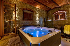 Ein Zimmer mit Stehwänden, einer Whirlwanne, Holzschränken und einer Glastür.