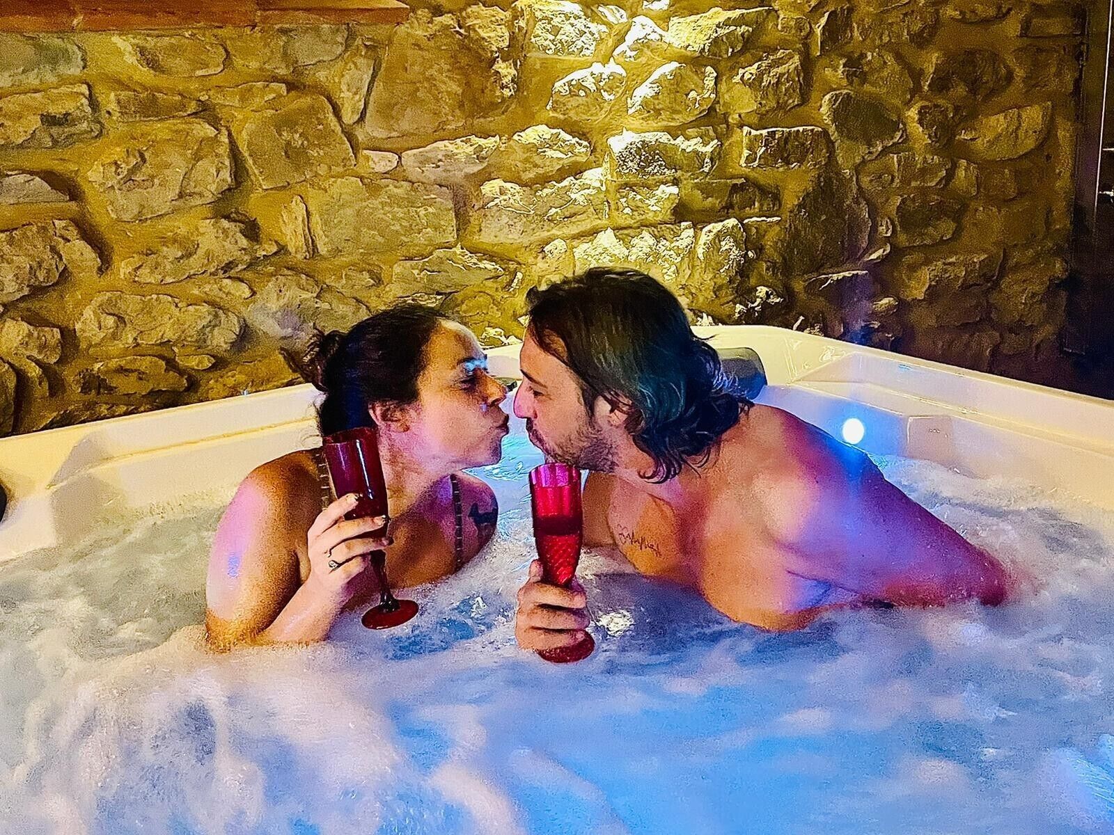 A couple in a hot tub with stone walls in the background.